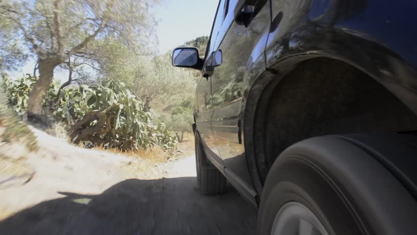 Large four by four drives off road through rugged terrain, seen from behind the rear wheel