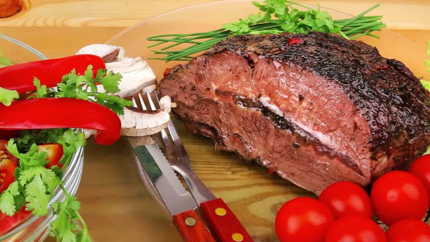 grilled beef sliced on transparent plate with salad bowl