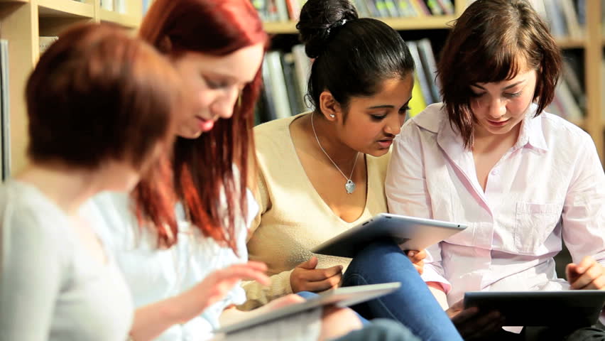 Group of diverse female students using online university internet on tablet computer in information library