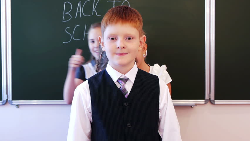 Group of successful schoolchildren giving thumb ups together in the classroom. Back to school is written on chalkboard. 