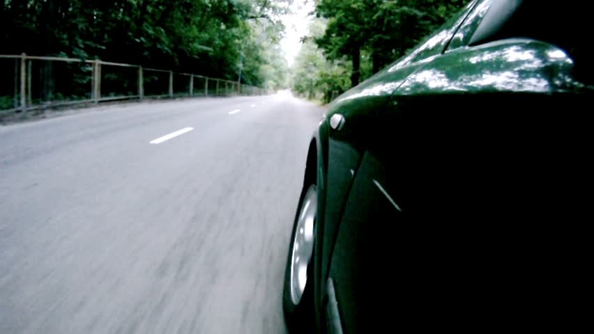 Car goes on asphalt road near trees in wood in afternoon