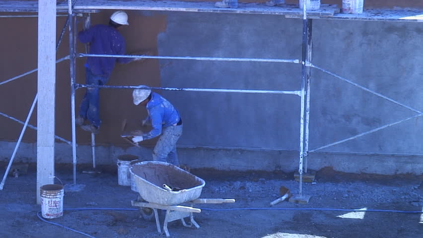 Stucco workers apply skin coat to building wall