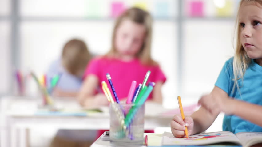 Cute little kindergarten child working at her desk is final focus of camera dolly movement.