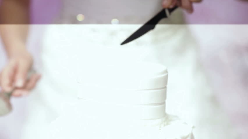 A groom and fiancee cut a wedding cake and lay it on a dish. CU.