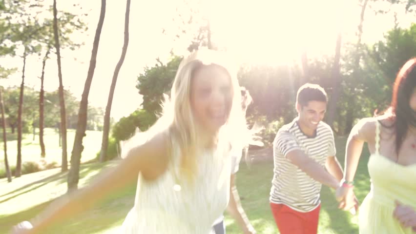 Four people holding hands as they run along country path.