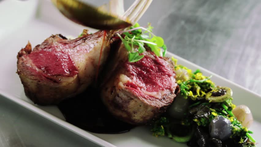 slide across a plate with lamb chops as Chef pours sauce on plate. Final touch.