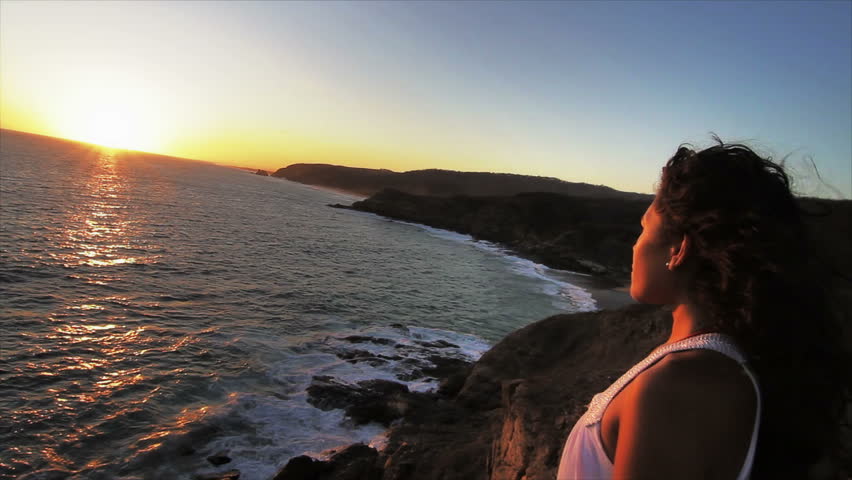 Woman watching the relaxing sunset over the cliff on the beach