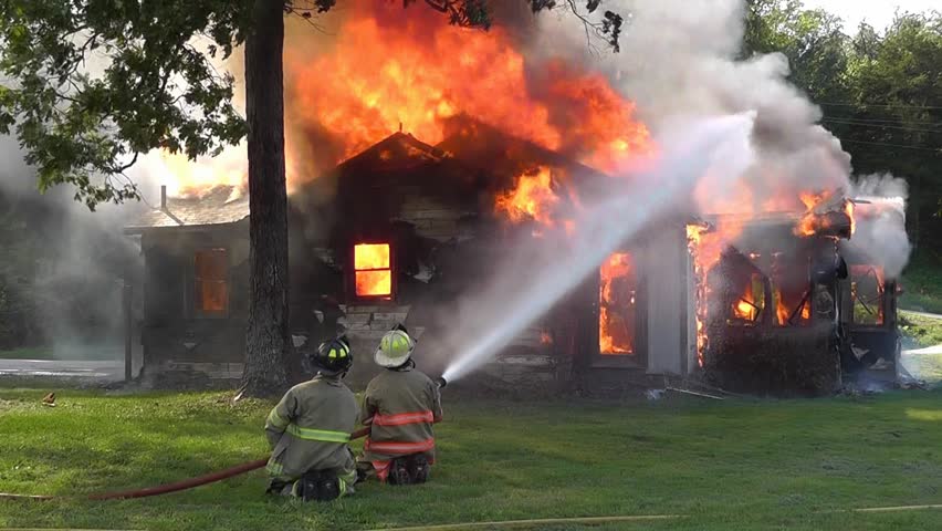 Firemen fight a blazing house fire with water from a high pressure hose in a control burn exercise.