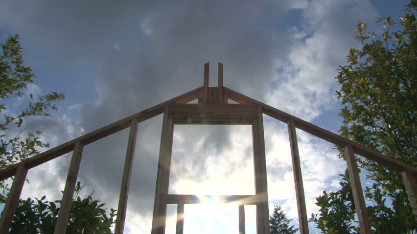 Time Lapse of clouds and sun shining through window on framework of new construction.