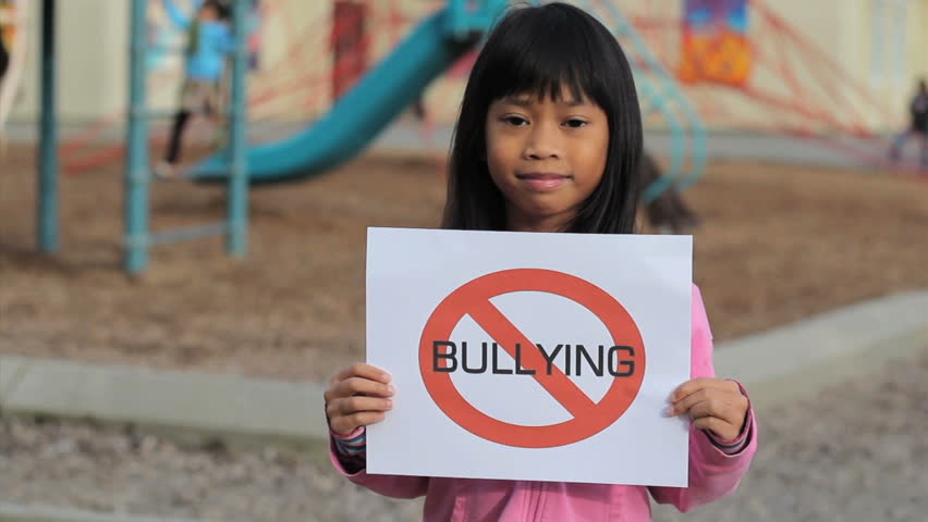A cute Asian girl holds up a large NO BULLYING sign on the school playground.