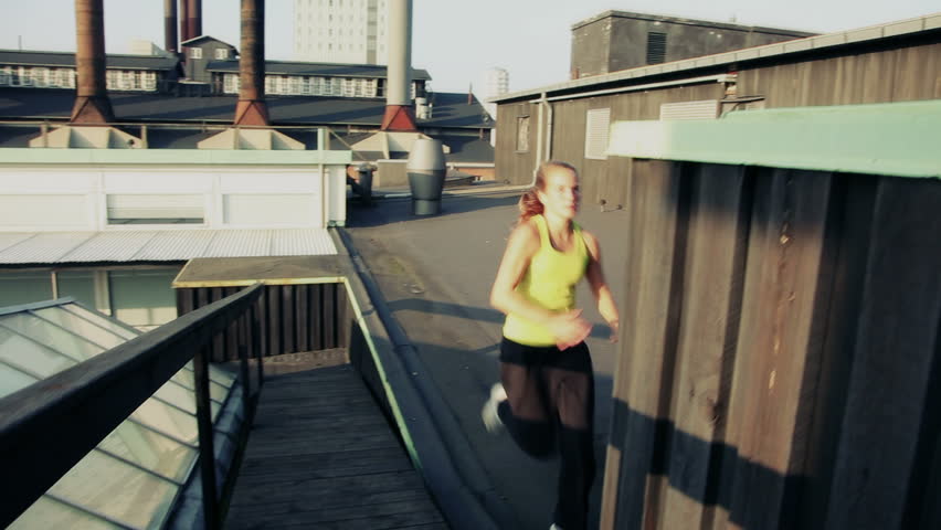Handheld shot of female doing parkour or free running flow on rooftop. Urban sunset scene.