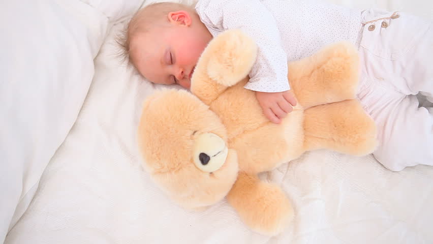 Baby sleeping with a teddy bear in a bedroom