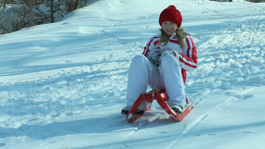Cheerful girl tobogganing down the hill and smiling at camera