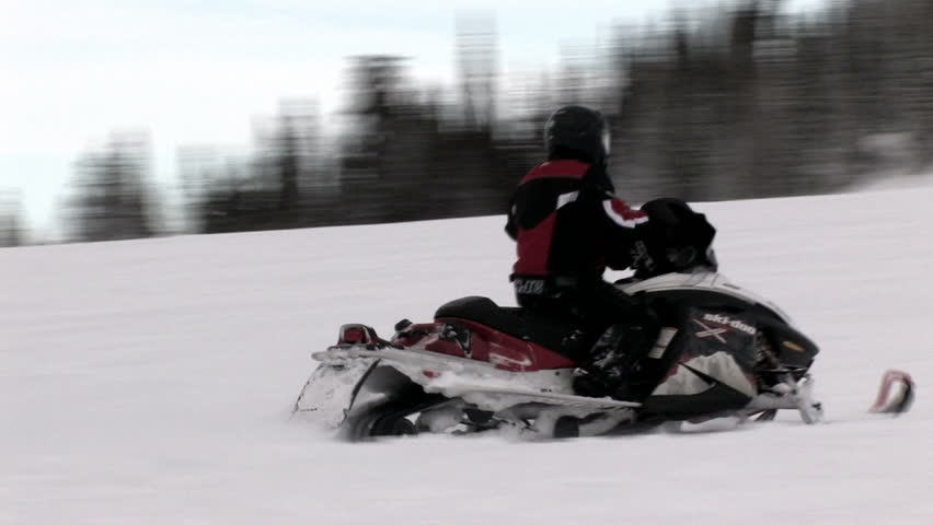 Snowmobile operator drives up a hill in central Utah. Rider wearing red and black as well as a safety helmet. Winter recreation. 