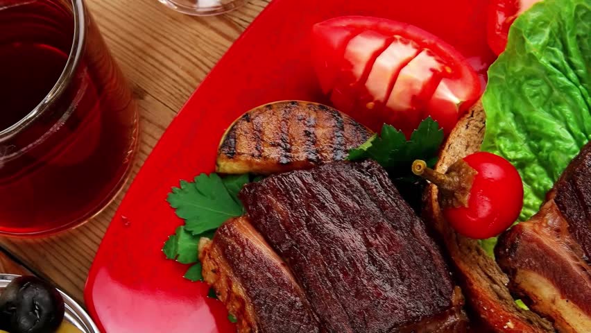 savory food : roast beef garnished with vegetables juice and olives on red plate over wooden table