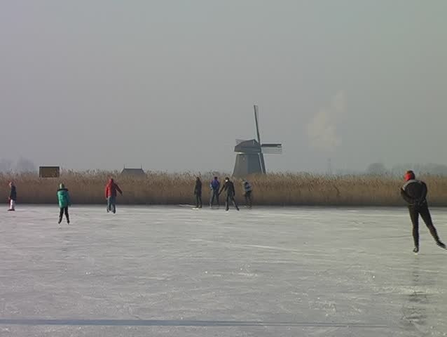 Typically dutch: ice skating on a frozen lake with view on a windmill on a cold winterday in the Netherlands