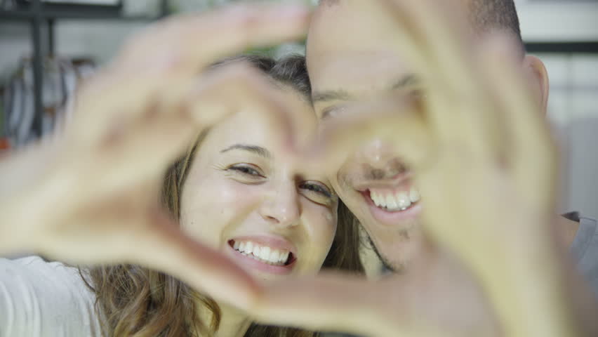 Close up of an attractive young mixed ethnicity couple who are laughing and making a heart shape with their hands. In slow motion.