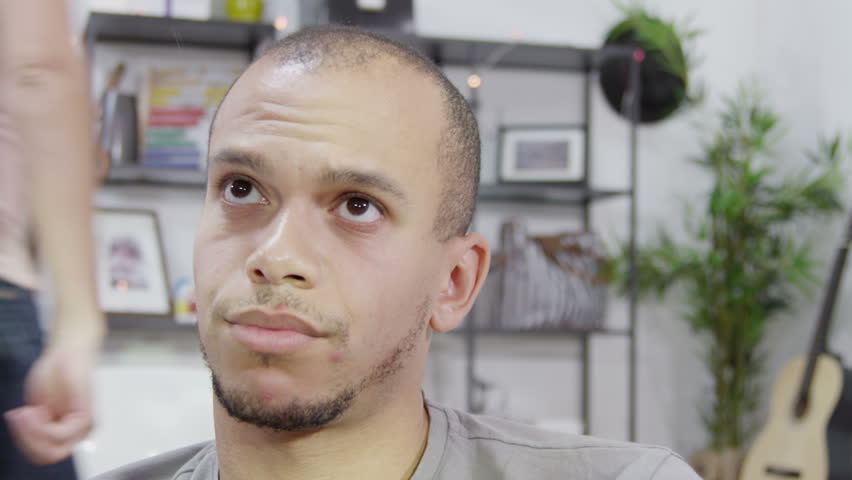 A man sits quietly and refuses to be drawn into an argument although we can see his partner in the background, pacing up and down and shouting
