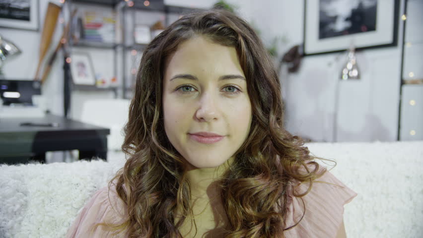Computer screen's point of view of young woman video chatting. Looking directly at camera for a close up shot and smiling and waving.