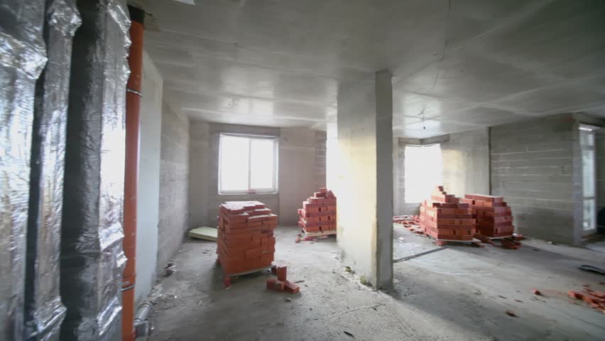 Piping and stacks of red bricks inside unfinished room with daylight from windows, panoramic motion