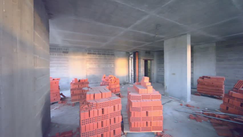 Piles of red bricks inside unfinished room lit by sun light from windows, shown in motion