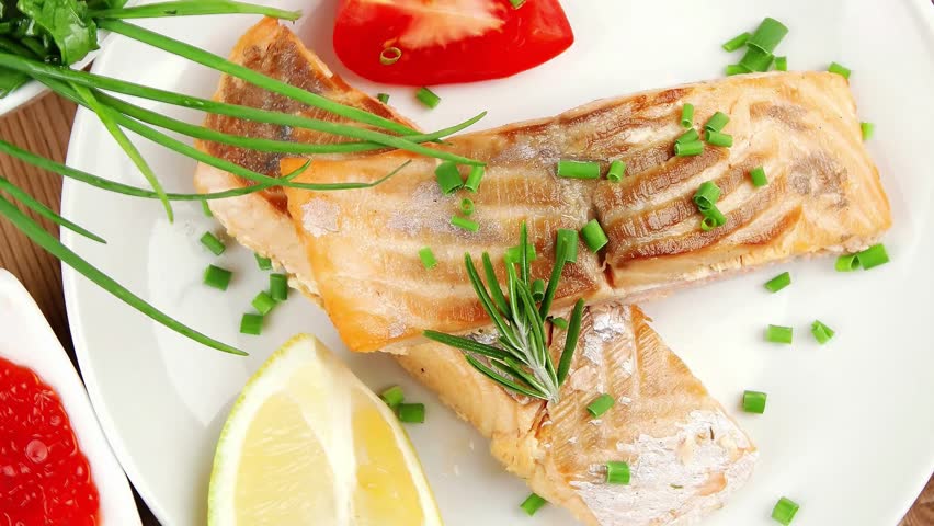 savory fish portion : roasted norwegian salmon chunks with lemon and vegetable salad rosemary twig and red caviar in white bowl over wooden table