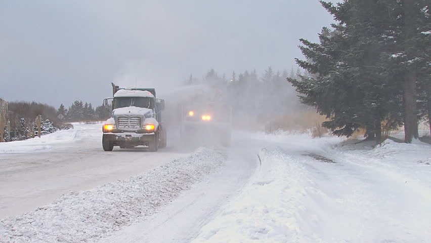 HOMER, AK - CIRCA 2011: Snow blower on an excavator paired with a dump truck to clean plow piles on snowy city street.