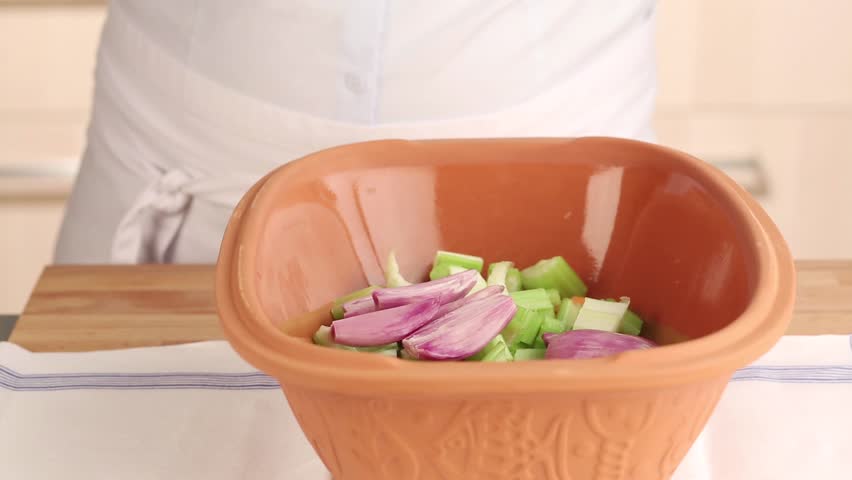 Herbs being added to vegetables in a terracotta baking dish