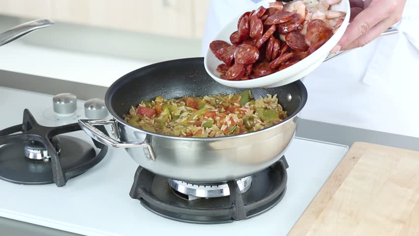 Jambalaya being made: sliced sausages and prawns being added to a rice and vegetable stew