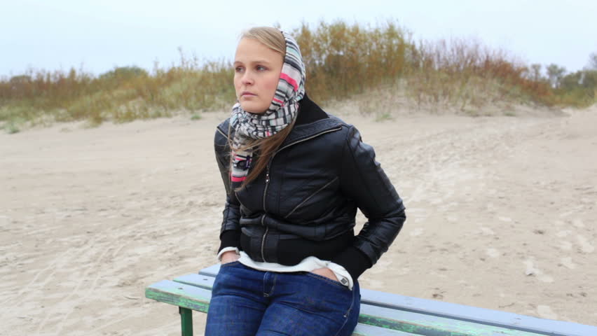 Young melancholy girl is sitting on a bench near the sea.