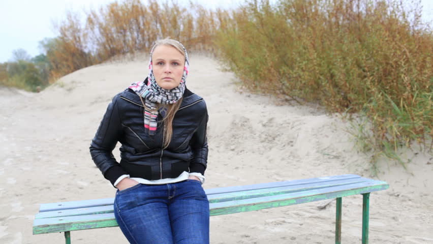 Young melancholy girl is sitting on a bench near the sea.