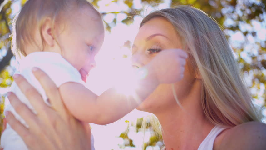 Young Caucasian mother outdoors holding her baby while he plays with her hair