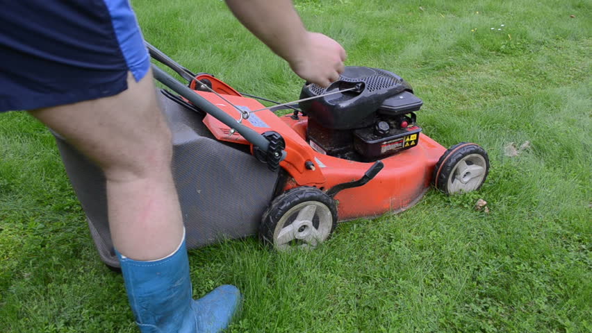 man gardener worker in shorts and blue rubber boots start grass lawn cutter mower and push