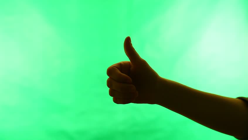 Young adult woman signals Ok!  against green screen chroma background. Back-lit silhouette.
