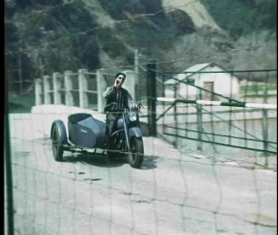 Man on old fashioned motorcycle with sidecar tossing cigarette butt