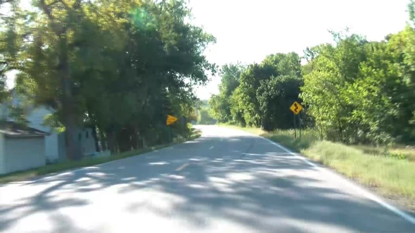 Winding road brings hood mounted camera between two lakes in Minnesota during summer with angled morning sunlight.