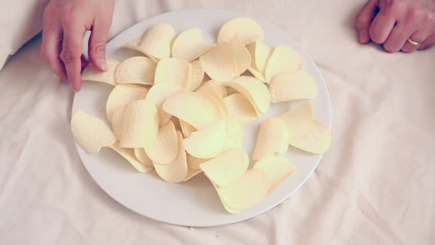 A dish full of unhealthy food, tasty potato chips. The hands of a man grab a potato chip.