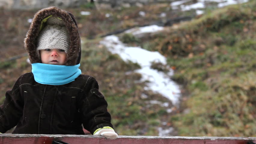 Cute baby standing on a bench and watching the winter scenery