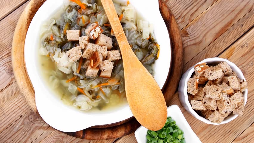 hot fresh diet vegetable soup with rye bread crackers over wood table on stand