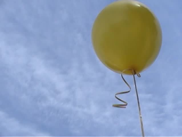 a yellow helium balloon floats away in the wind against a blue spring sky