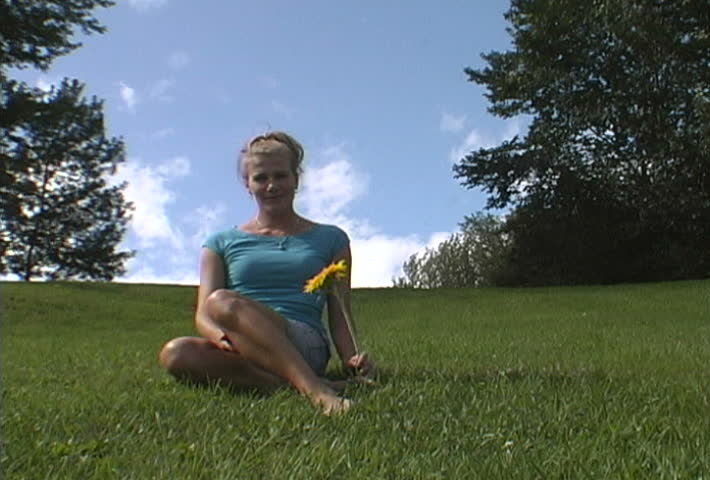 Video of a girl holding a big yellow flower in a park with plenty of space to ad your own elements.