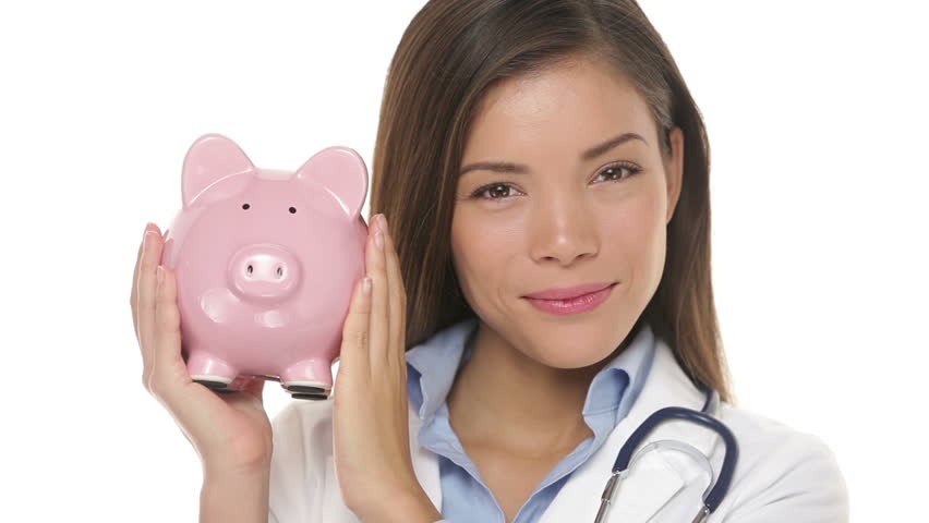 Sad woman doctor holding piggy bank in EXPENSIVE HEALTH CARE concept video. Multiracial young female medical professional indicating no money on white background wearing medical uniform lab coat.