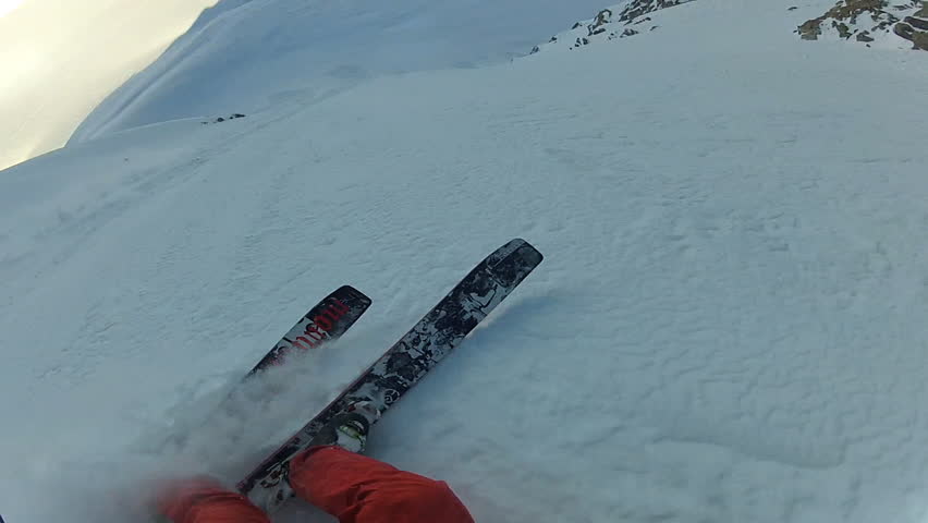 A skier carves back and forth as he rides down a mountain covered in fresh powder during the day. It is shot with a camera mounted to the athletes head and provides a POV, point of view, perspective.