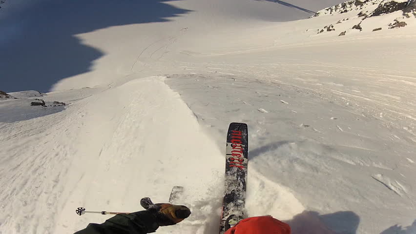 A skier carves back and forth as he rides down a mountain covered in fresh powder during the day. It is shot with a camera mounted to the athletes head and provides a POV, point of view, perspective.
