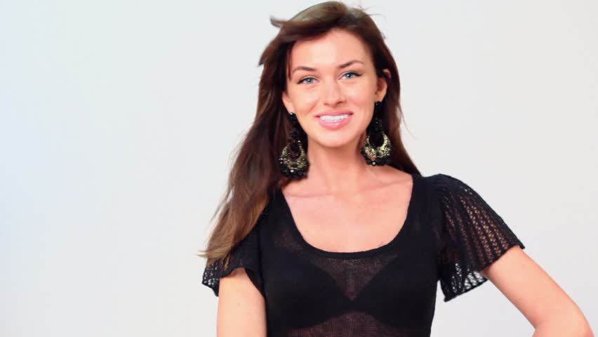 Happy girl with huge earrings poses in transparent dark blouse and black bra, wind blows her hair