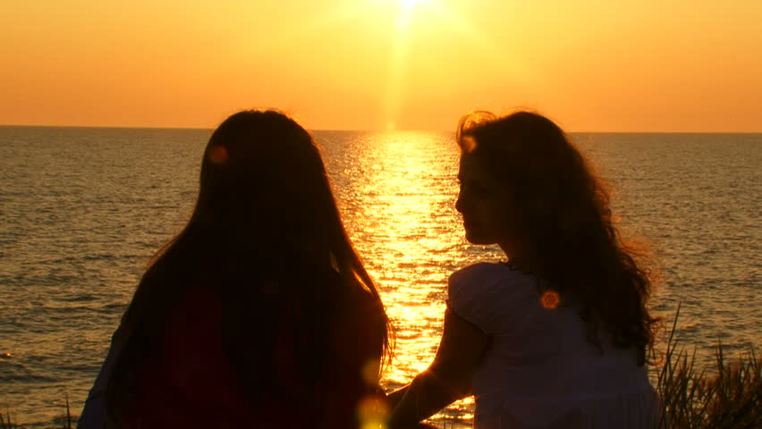 Two friends talking on the beach at sunset.