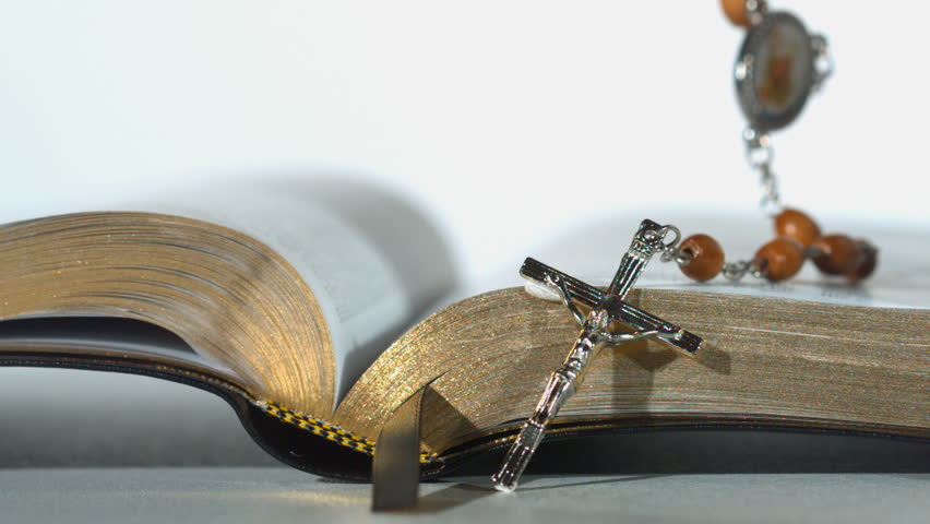 Rosary beads falling on open bible on white background close up in slow motion