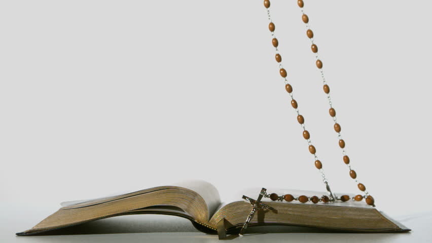 Rosary beads falling onto open bible on white background in slow motion