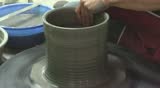 Two hands are molding clay into a vase.