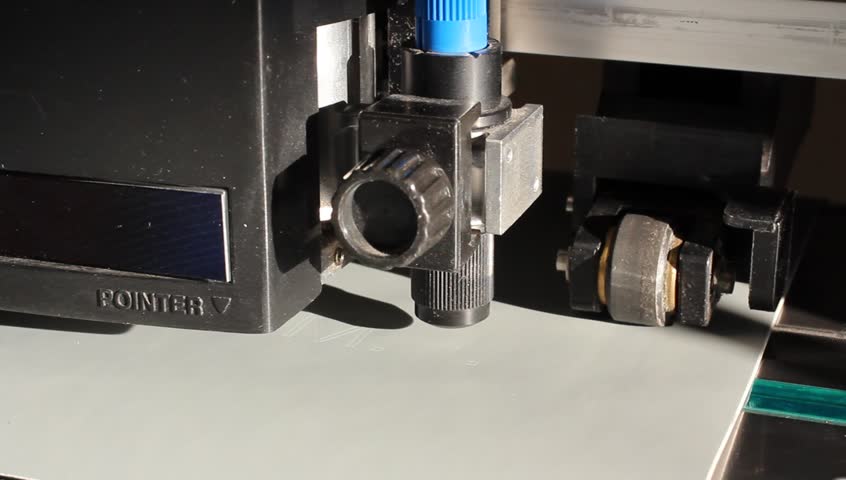 Cutting plotters use knives to cut the letters on gray vinyl film. Three-quarter view close-up